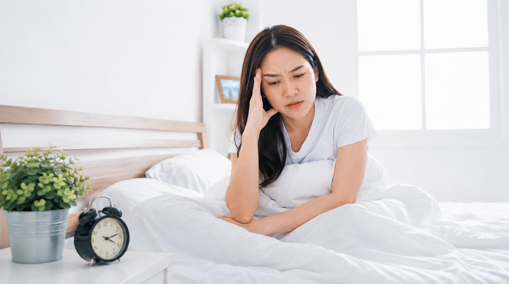 Người phụ nữ ngồi trên giường, tay ôm đầu vì lo lắng và khó ngủ